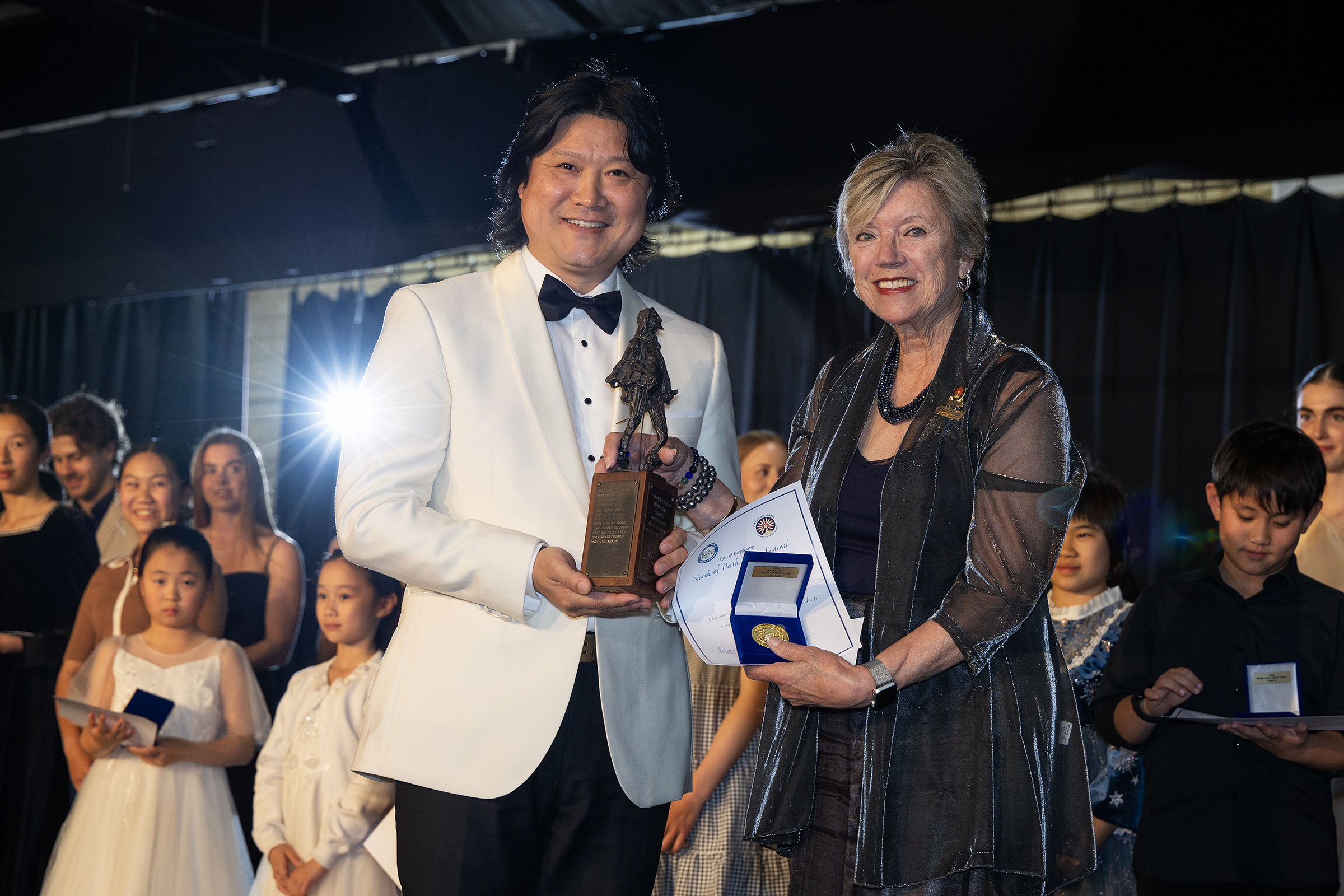A winner in a white jacket receives a trophy from a presenter.