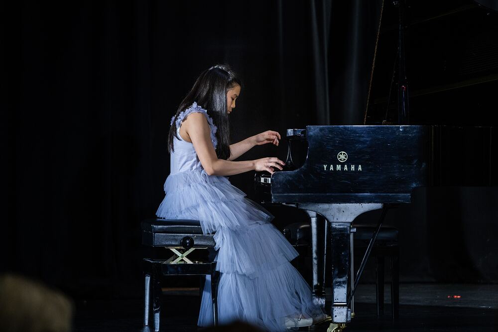 A young pianist in a pale blue tulle dress plays the grand piano.