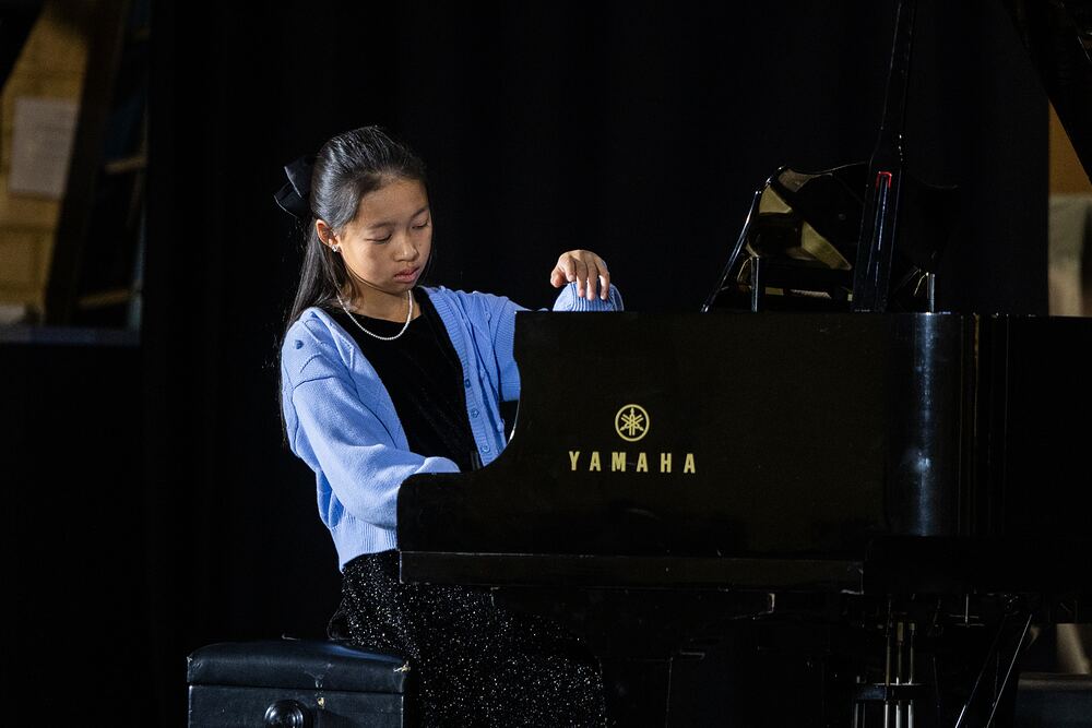A young pianist in a blue cardigan plays the grand piano.