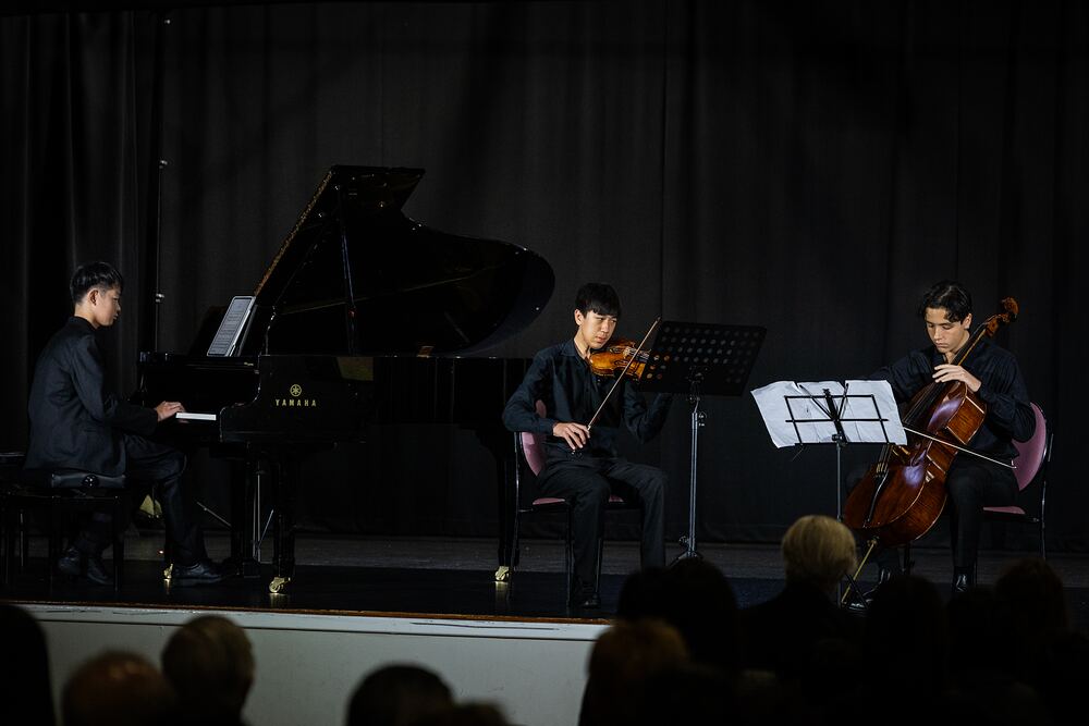 A piano trio of piano, violin and cello performs for the audience.