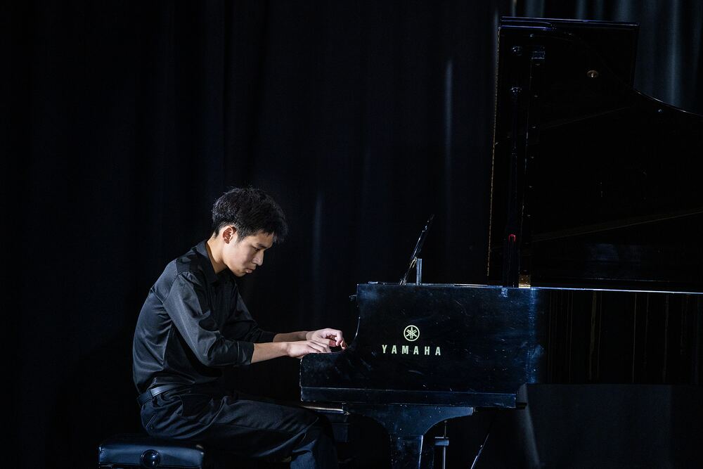 A young pianist dressed in black plays the grand piano.