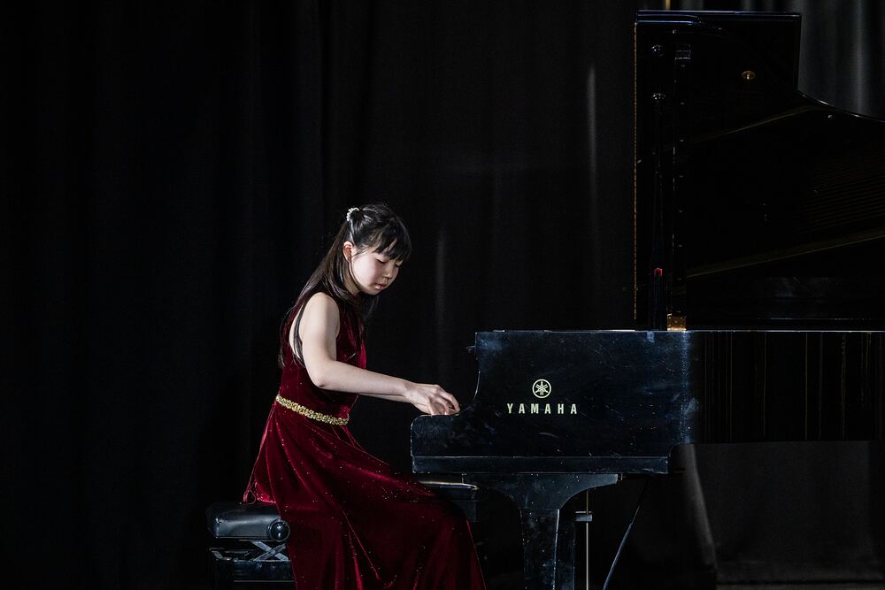 A young pianist in a red velvet dress plays the grand piano.