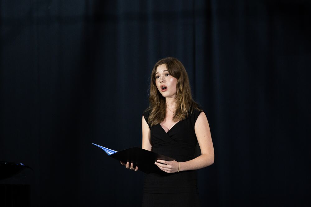 A singer in a black dress performs, holding her music folder.