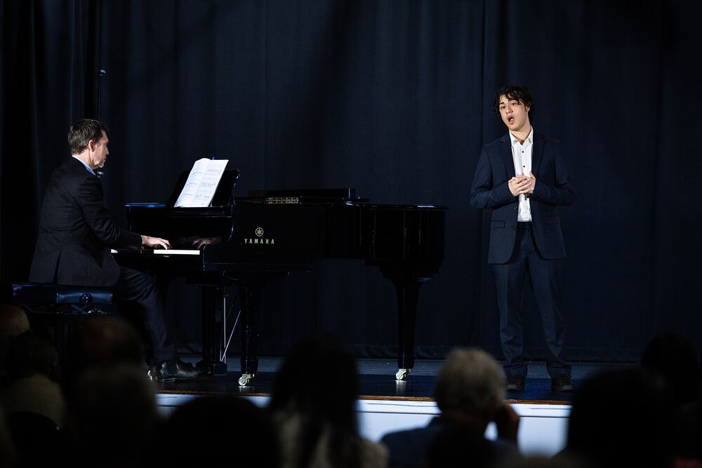 A young singer performs centre stage, a pianist accompanying him.