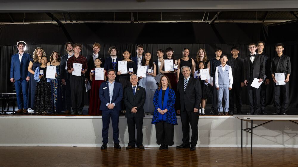 The concert's award winners stand together on stage holding certificates, Festival officials in front.