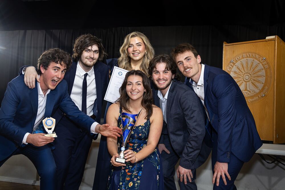 Smiling winners pose together with their trophies beside the lectern.