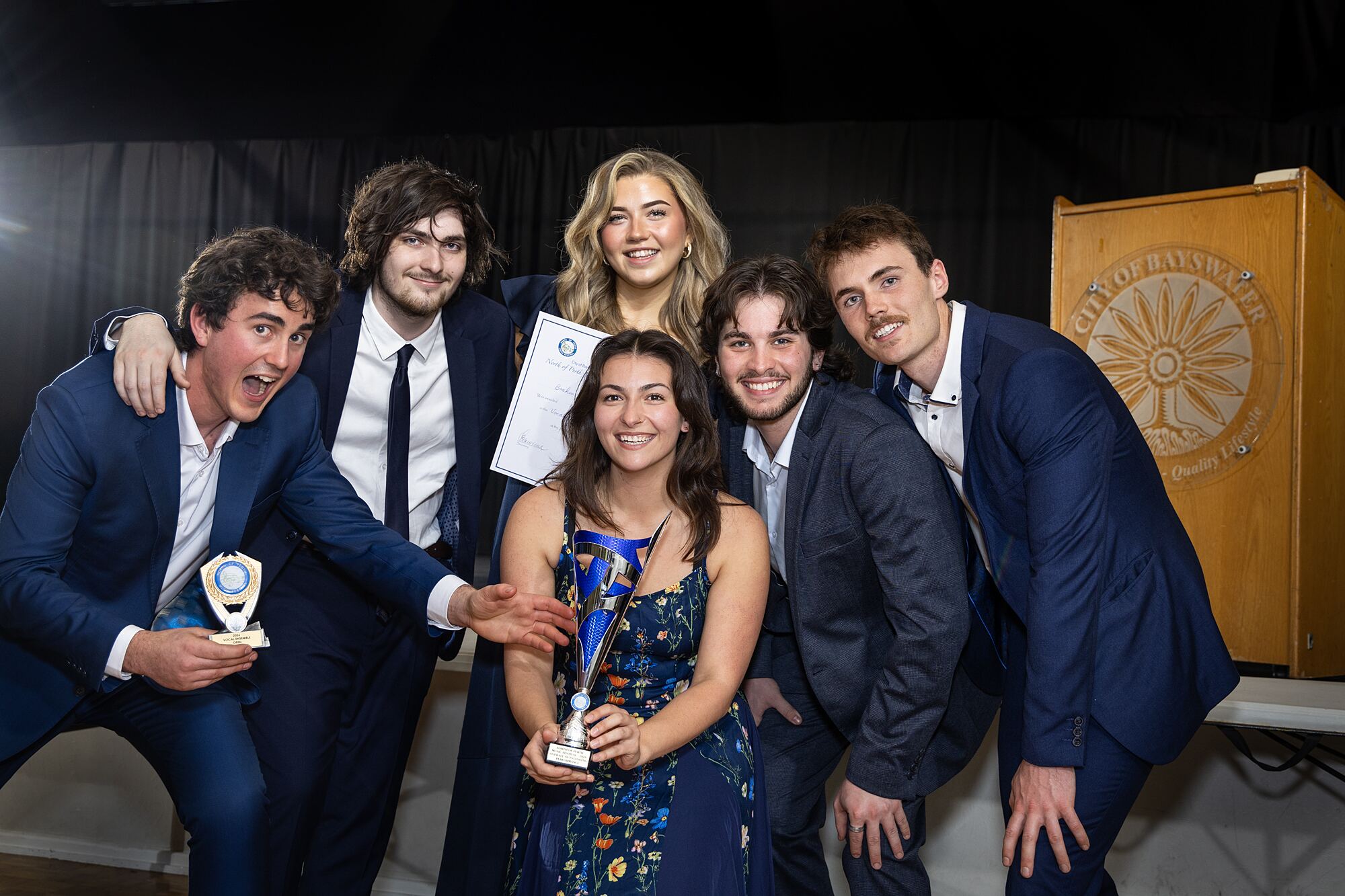 Smiling winners pose together with their trophies beside the lectern.