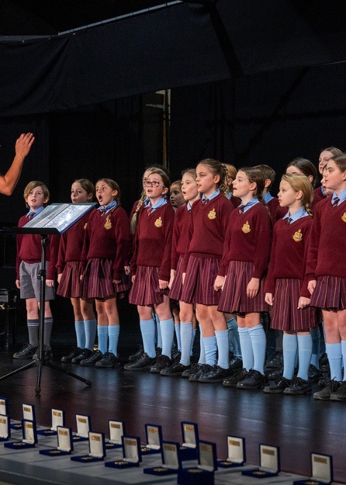 A choir performs, with medallion boxes lined up in front of the stage.