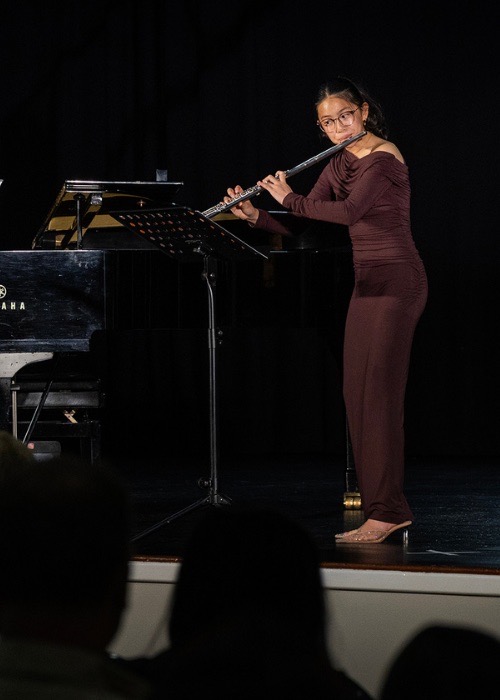 A flautist performs a solo beside a grand piano.